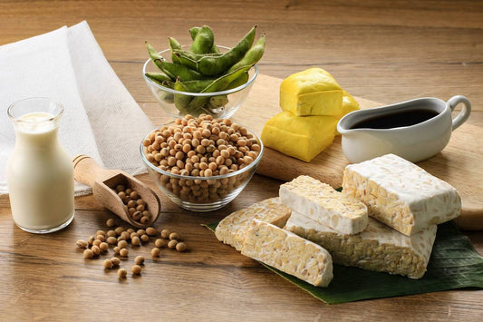 produkty z soi, tofu, tempeh, mleko sojowe, sos sojowy, ziarna soi, rozłożone obok siebie na drewnianym stole